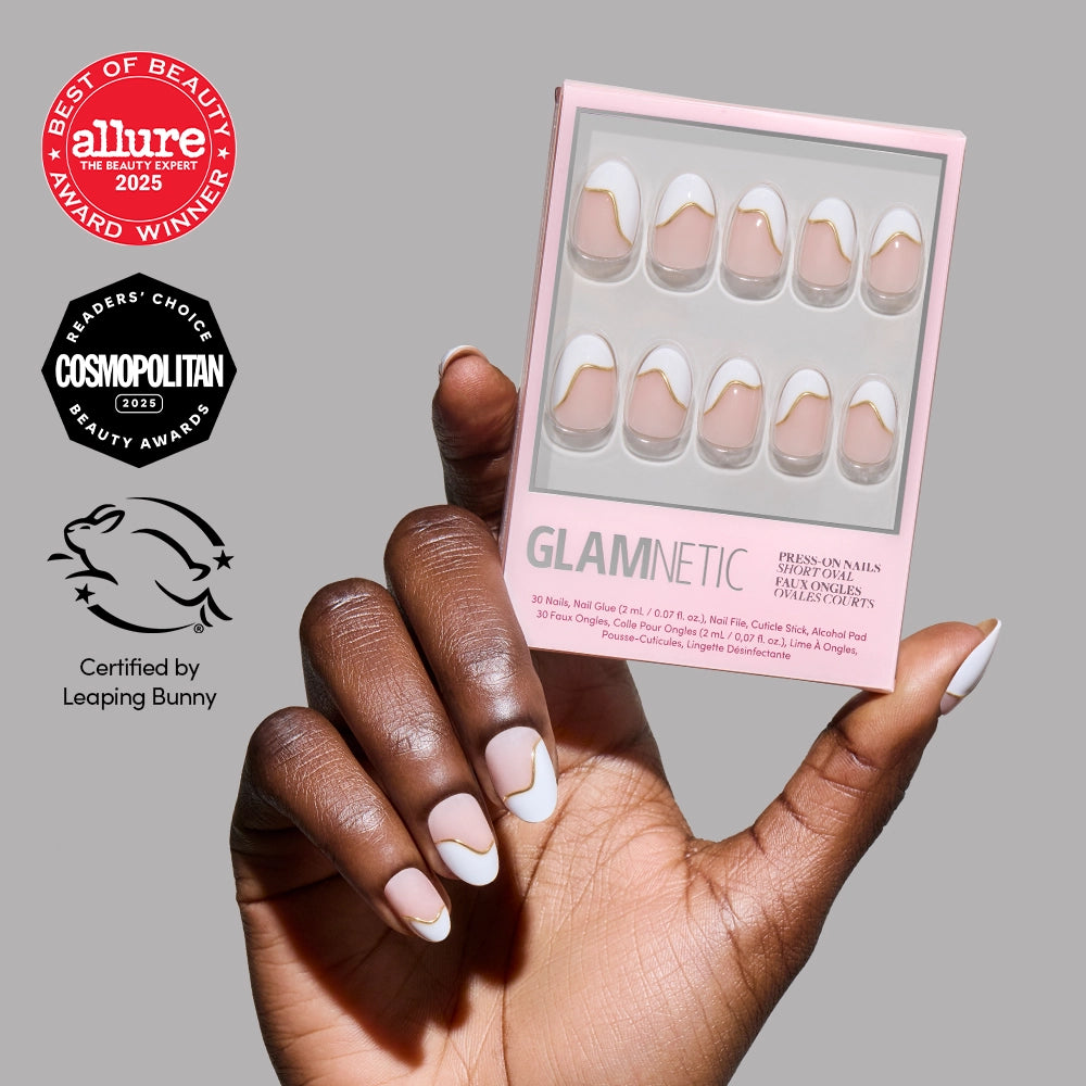 A hand with neatly manicured, almond-shaped nails in a white and nude abstract style holds a glamnetic French Muse press-on nails box. Beauty award icons and a cruelty-free certification appear on the left.