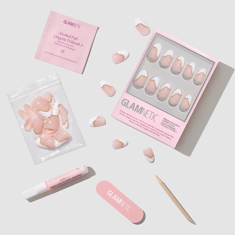 The French Muse press-on nails by glamnetic include pink and white nails, a pink nail file, wooden cuticle stick, nail glue, alcohol pad, and extra nails for a salon-quality mani—all displayed on a light gray surface. - Product image