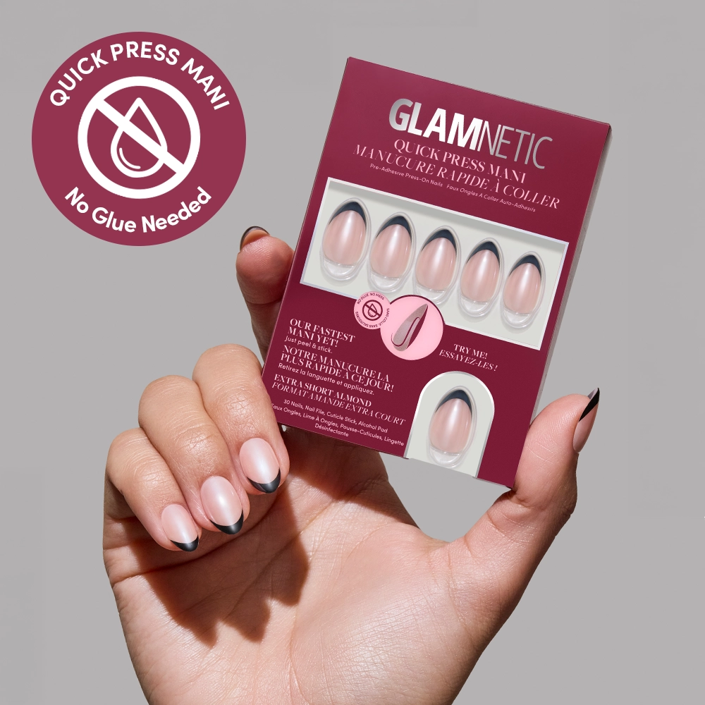 A hand with short, almond-shaped nails in black French tips holds a glamnetic French Noir Quick Press Mani box. A circular label reads, No Glue Needed—perfect for easy, mess-free nails.