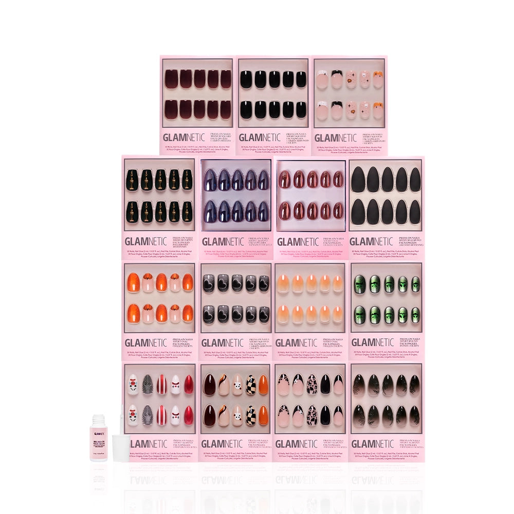 Sixteen sets of glamnetic’s Fright Night Collection press-on nails in pink packaging are arranged in a grid, featuring haunted glamour colors and designs, with a small nail glue bottle displayed at the front left. - Product image