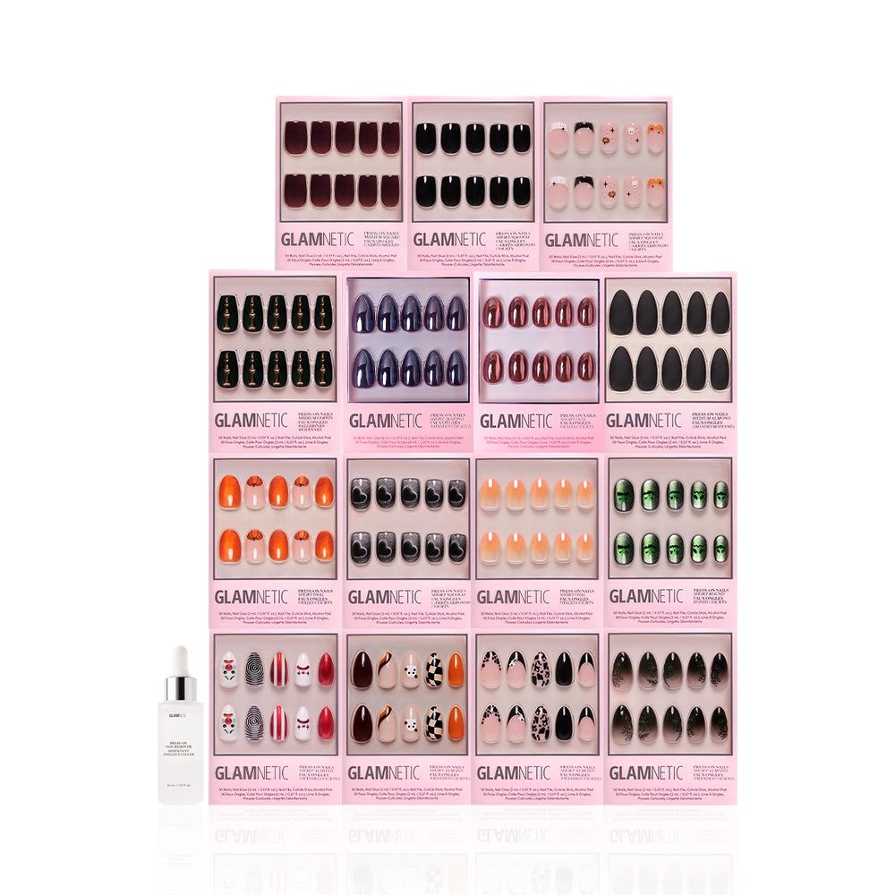 Fourteen Glamnetic press-on nail sets from the Fright Night Collection in various colors and designs, arranged above a bottle of Glamnetic nail glue on a white background. - Product image