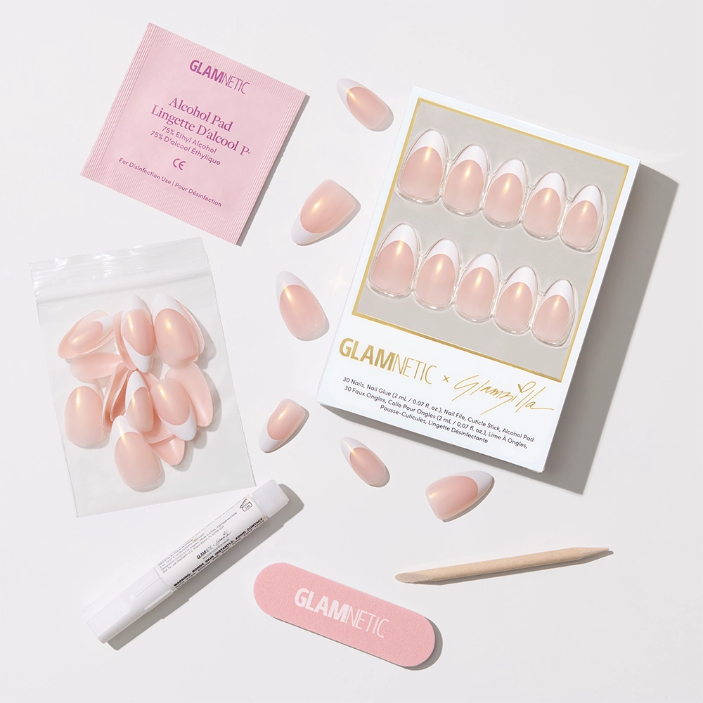 Flat-lay of the complete nail kit: boxed press-on nails, loose extra nails in a pouch, nail glue pen, alcohol pad, pink Glamnetic nail file, and wooden cuticle stick—all arranged on a bright white surface.
- Product image