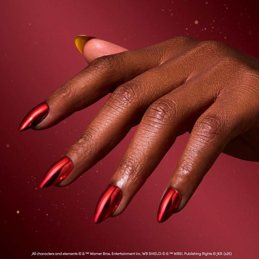 A hand with long, almond-shaped, glossy red chrome nails is shown against a matching red background, elegantly displaying glamnetic's Godric Gryffindor™ Nail Set. - Product image