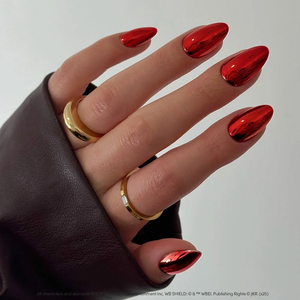 A hand with long, chrome almond nails in the bold, red metallic Godric Gryffindor™ shade by glamnetic, adorned with two gold rings and partly hidden by a dark sleeve. - Product image