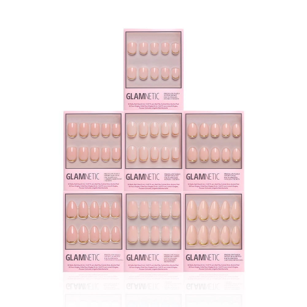Seven boxes of the glamnetic Gold Girlie Bundle press-on nails are stacked in a pyramid against a white background, each showcasing a range of nail shapes and sizes through a clear window. - Product image