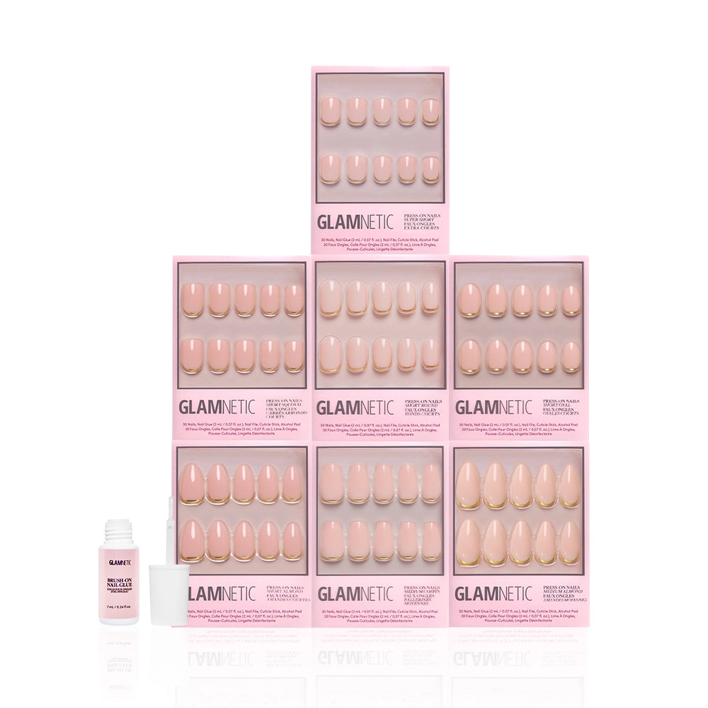 Nine boxes of glamnetic's Gold Girlie Bundle press-on nails are stacked in a pyramid, with a small bottle of glamnetic brush-on nail glue in front on the left, all set against a white background. - Product image