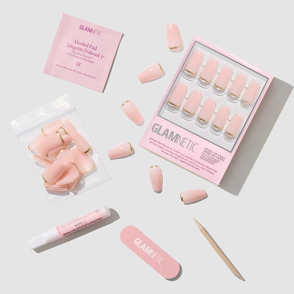 The glamnetic Gold Goals set features pink coffin-shaped press-on nails with gold tips, a nail file, cuticle stick, nail glue, alcohol pad, and extra nails—all arranged on a light gray background for salon-quality manis at home. - Product image