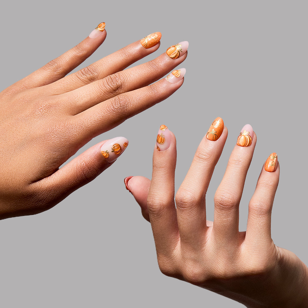 Two hands are shown against a light grey background, featuring short oval nails wearing glamnetic’s Golden Gourds press-ons—a clear base adorned with small, 3D golden pumpkin accents that are perfect for a fall or Halloween aesthetic. - Product image