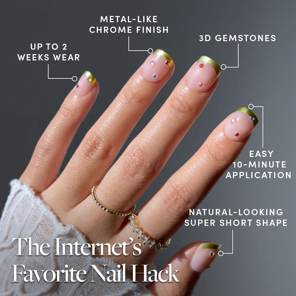 A hand wears Glamnetic Goodie Gumdrops, featuring nude-toned vegan press-on nails with metallic chrome French tips and small gemstones, designed for a 10-minute application and up to two weeks of wear. - Product image