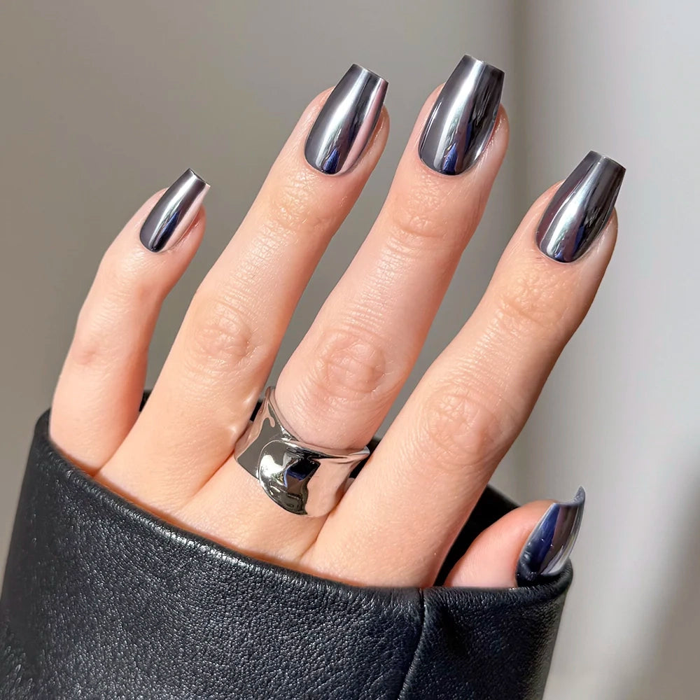 A hand with slightly spread fingers wears glamnetic Gunmetal coffin-shaped press-on nails in a shiny, gunmetal chrome finish, paired with a silver ring and a black sleeve, reflecting light. - Product image