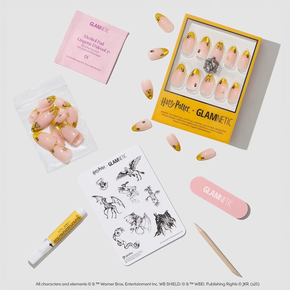 The glamnetic Helga Hufflepuff™ Nail Set features pink, gold, and yellow velvet French tip press-ons with nail glue, an alcohol pad, nail file, and a magical creatures sticker sheet—all arranged on a light surface. - Product image
