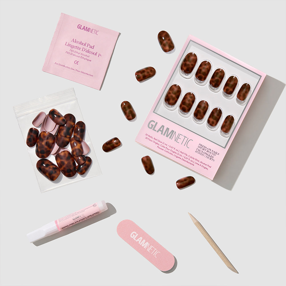 A set of glamnetic Hidden Fortune short round tortoiseshell press-on nails is shown with a nail file, cuticle stick, nail glue, alcohol pad, and extra nails arranged neatly on a white background for a salon-quality manicure at home. - Product image