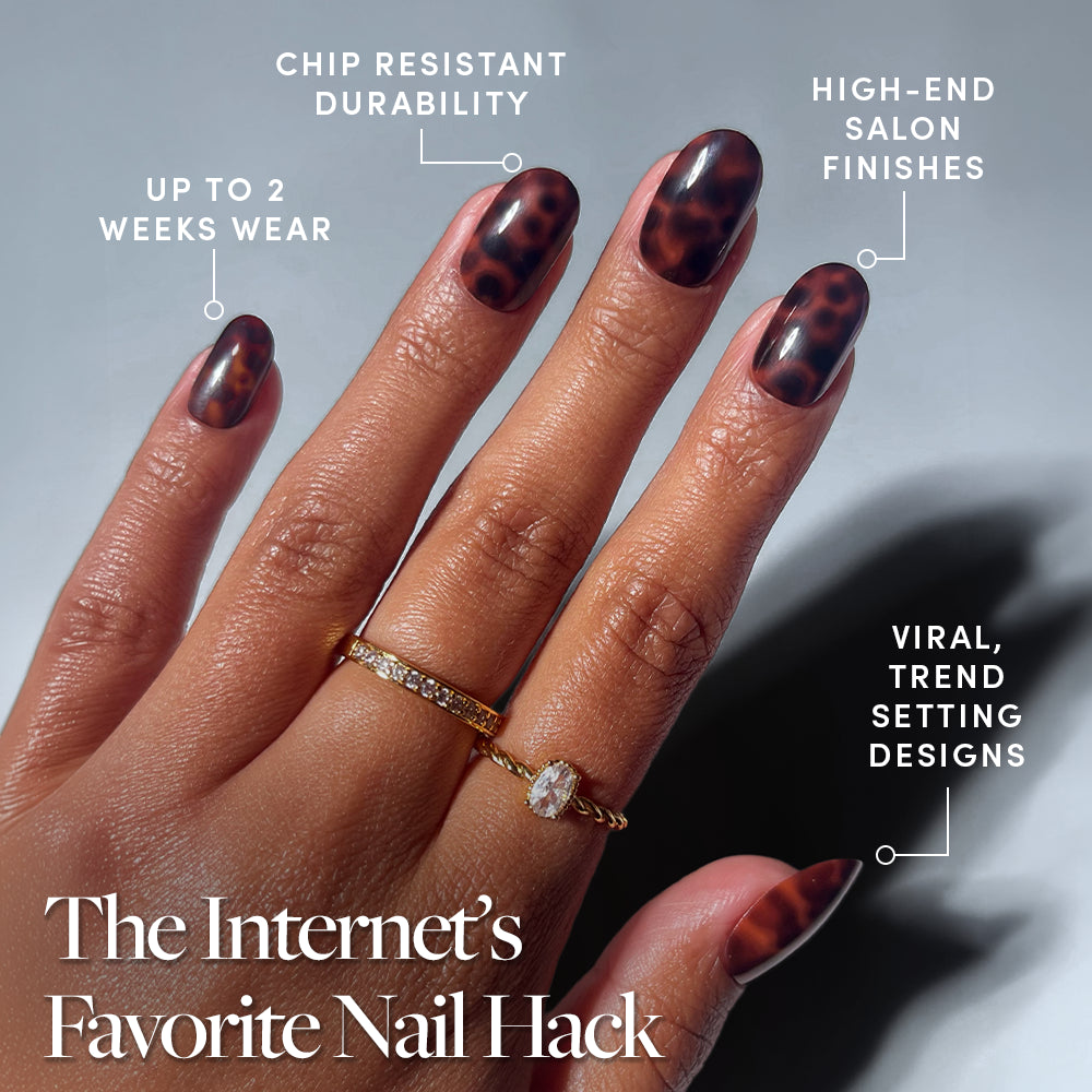 A hand with short, almond-shaped "Hidden Fortune" press-on nails by glamnetic in brown and black tortoiseshell, wearing two gold rings. Features include up to 2 weeks of durable, salon-quality wear and trendy viral designs. - Product image