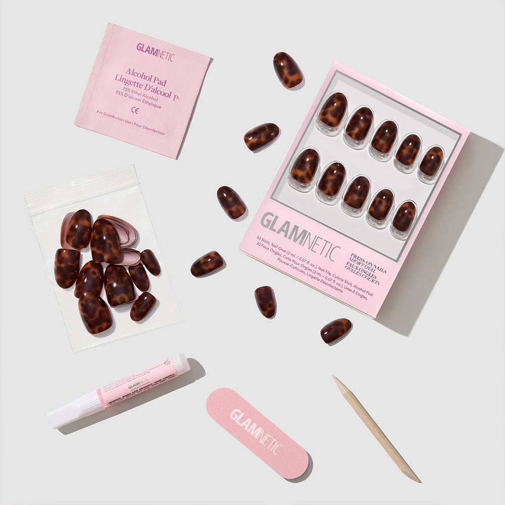 A flat lay of the Glamnetic High Society kit shows short oval tortoiseshell press-on nails with essentials—nail file, cuticle stick, alcohol pad, glue, and extra nails—for a salon-quality manicure on a white background. - Product image
