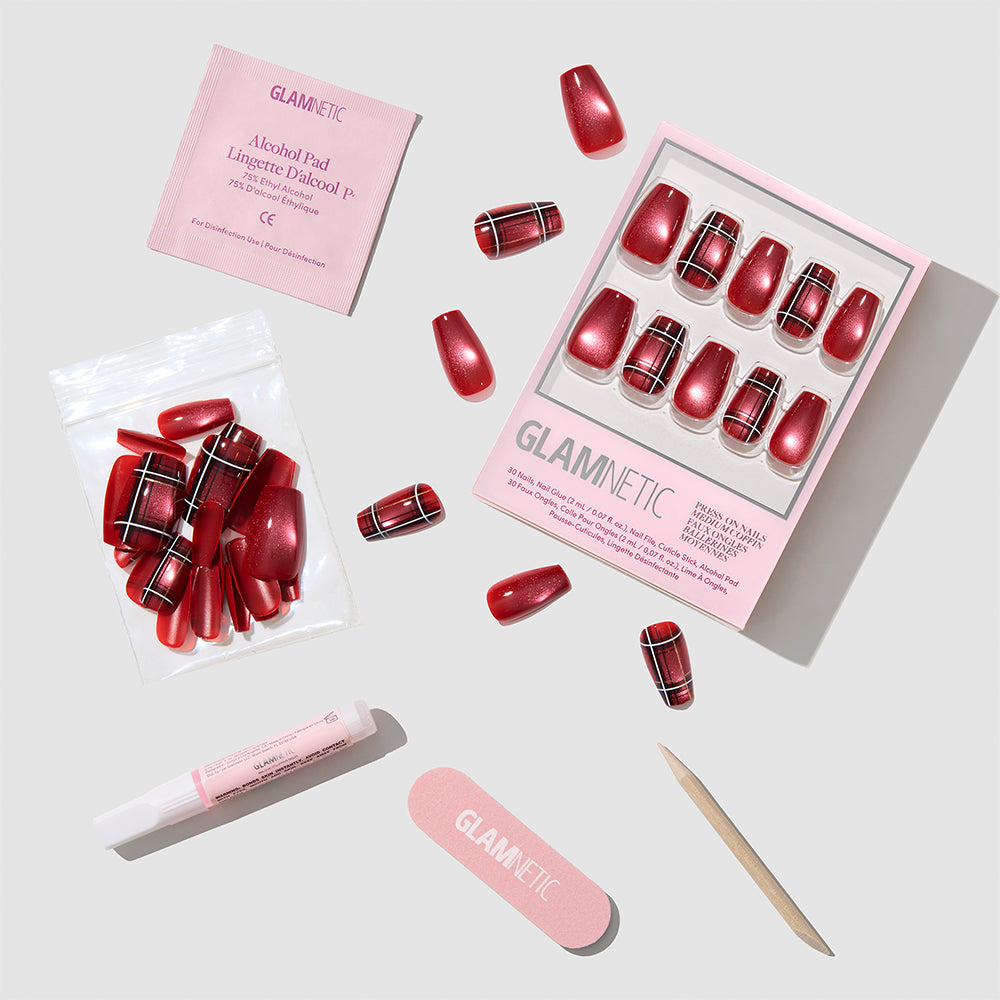 A set of glamnetic Holiday Tartan Press-On Nails in vibrant red plaid, complete with glue, a pink nail file, wooden cuticle stick, alcohol pad, and extra nails—all arranged neatly on a light background. - Product image