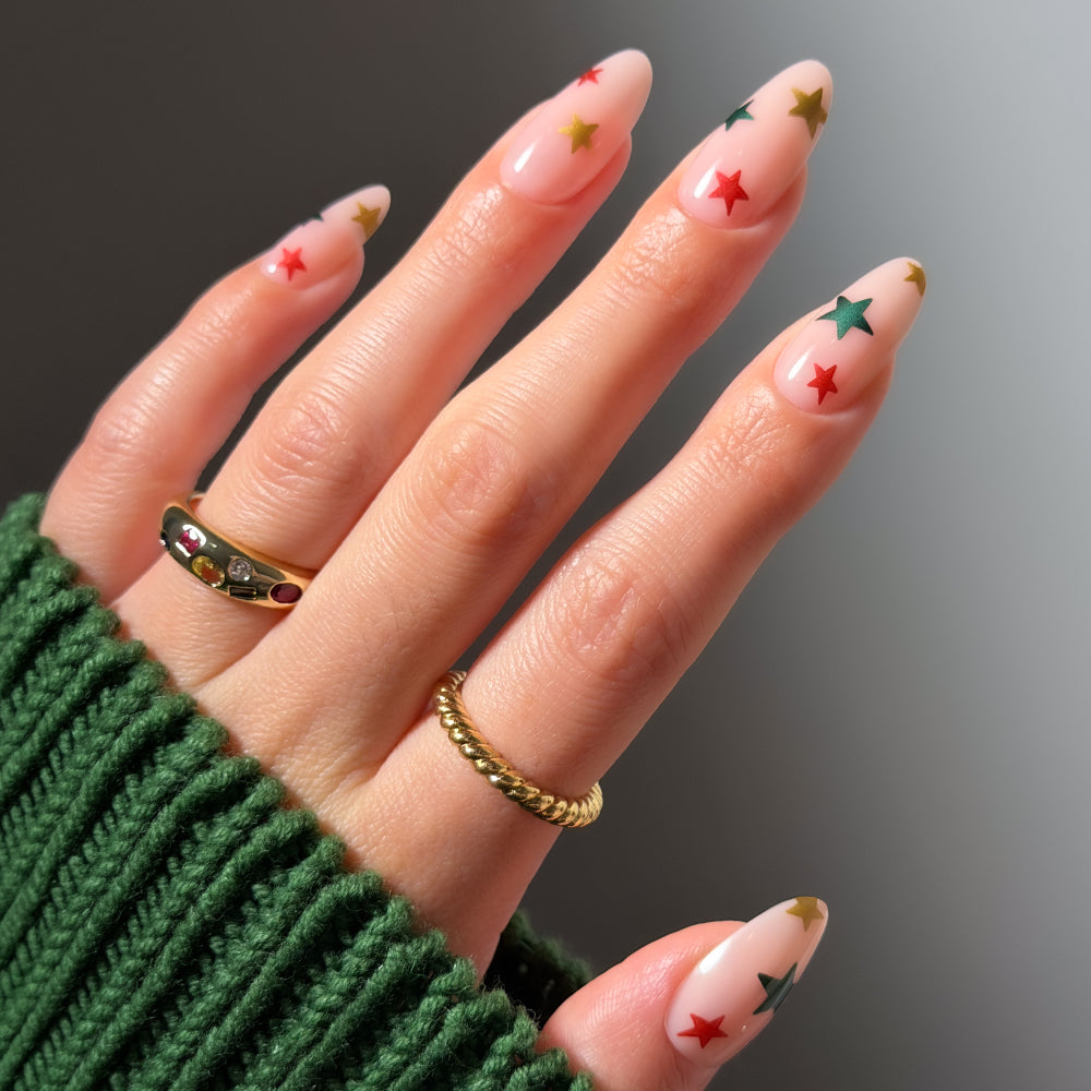 Holiday Wish almond-shaped salon-quality manicure featuring a clear base with small red, green, and gold star designs.