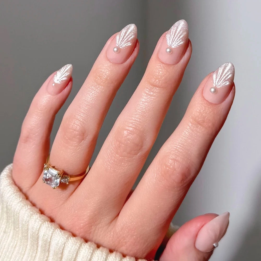 Honeymoon - Glamnetic Honeymoon short almond press-on nails featuring a light pink base with white shell-patterned art and small pearl accents at the base of each nail.