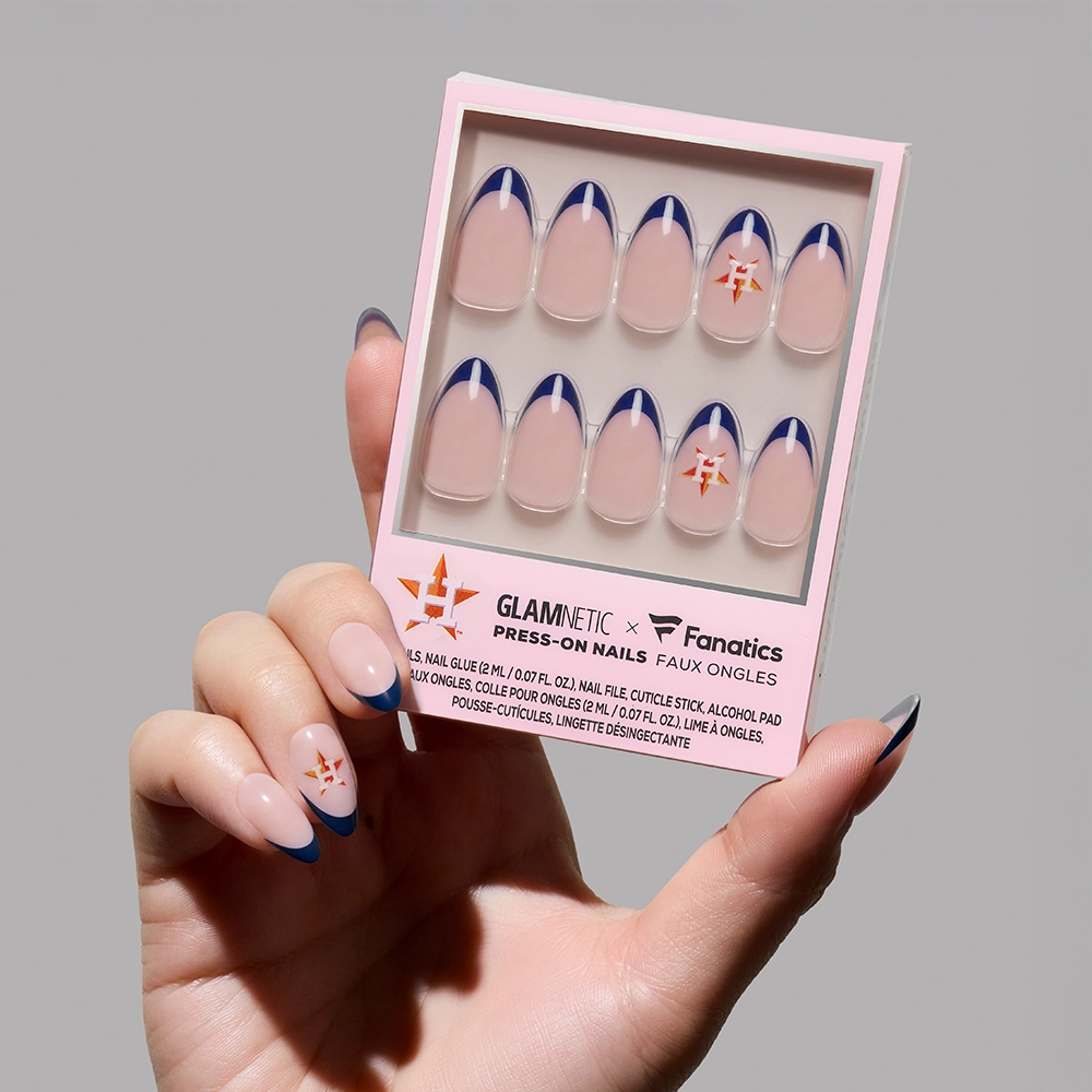 A hand holds the glamnetic Houston Astros Press-On Nail Set, featuring a nude base with blue French tips and orange star-accent nails—perfect for stylishly showing your team spirit.