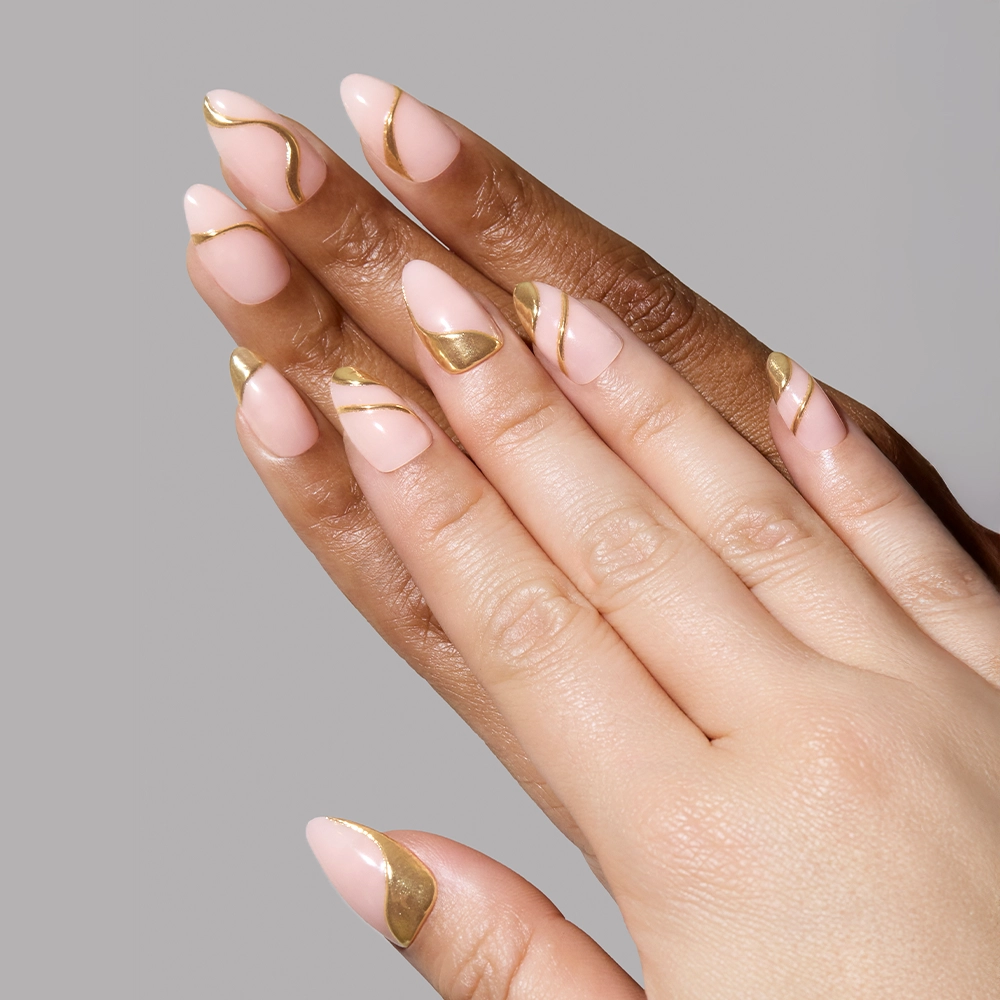 Two hands—one light-skinned and one dark-skinned—displaying the same Glamnetic x Glamzilla press-on nails. The nails have a glossy pink base with bold metallic gold curves, showcasing their versatility across different skin tones.
- Product image