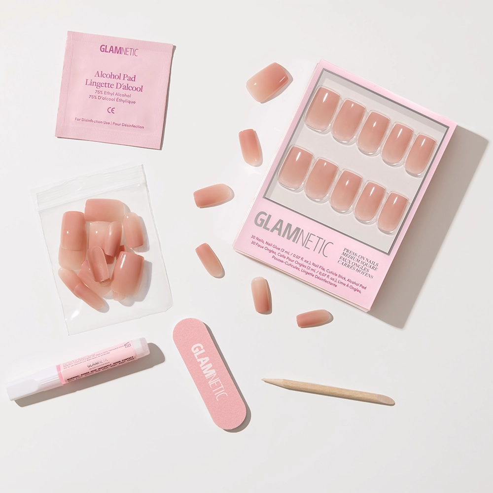 The glamnetic In The Nude set includes nude-pink ombré press-on nails in a pink case, plus a nail file, cuticle stick, glue, alcohol pad, and extra nails—everything needed for an easy minimalist manicure. - Product image