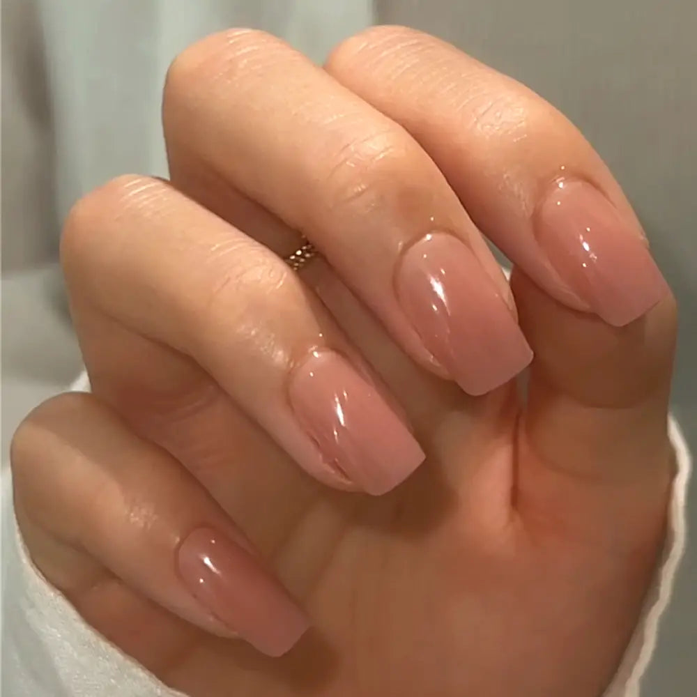 A hand with neatly manicured, glossy nude-pink ombré medium square nails, featuring the “In The Nude” press-on set from glamnetic, held against a light background. - Product image