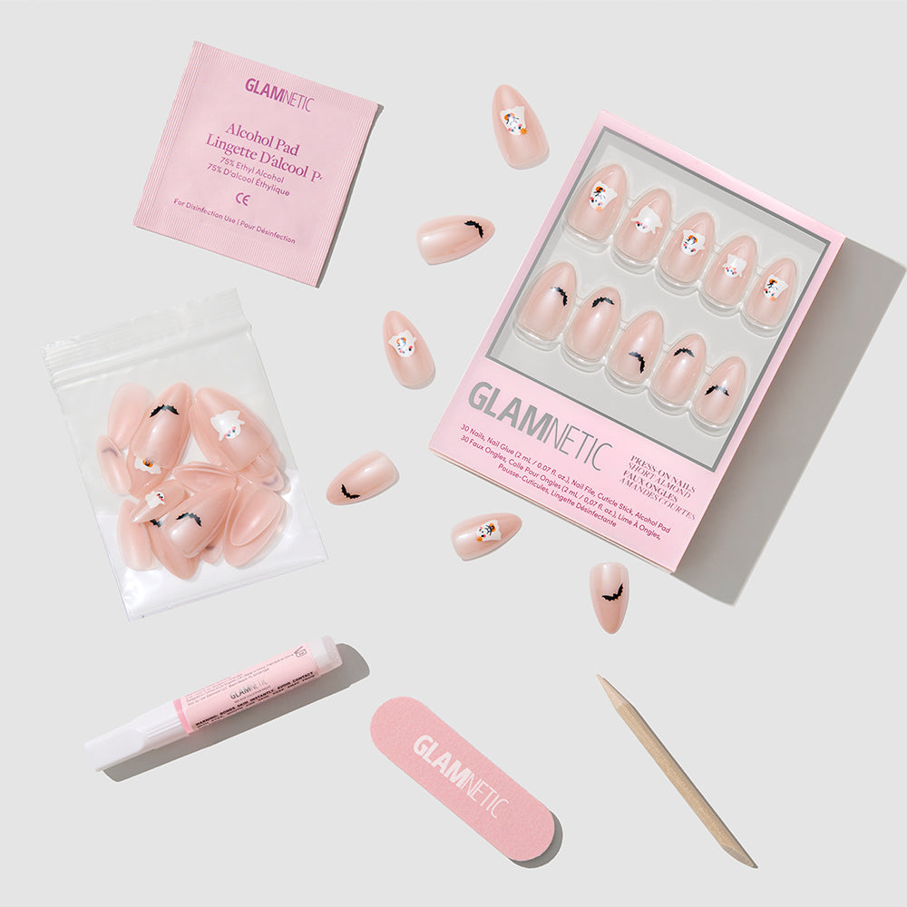 The “In The Spirit” press-on nails by glamnetic feature a pink, short almond shape adorned with adorable bear designs and a subtle glazed finish. The set includes an alcohol pad, nail glue, a small nail file, a cuticle stick, and extra nails, all arranged neatly on a white surface. - Product image