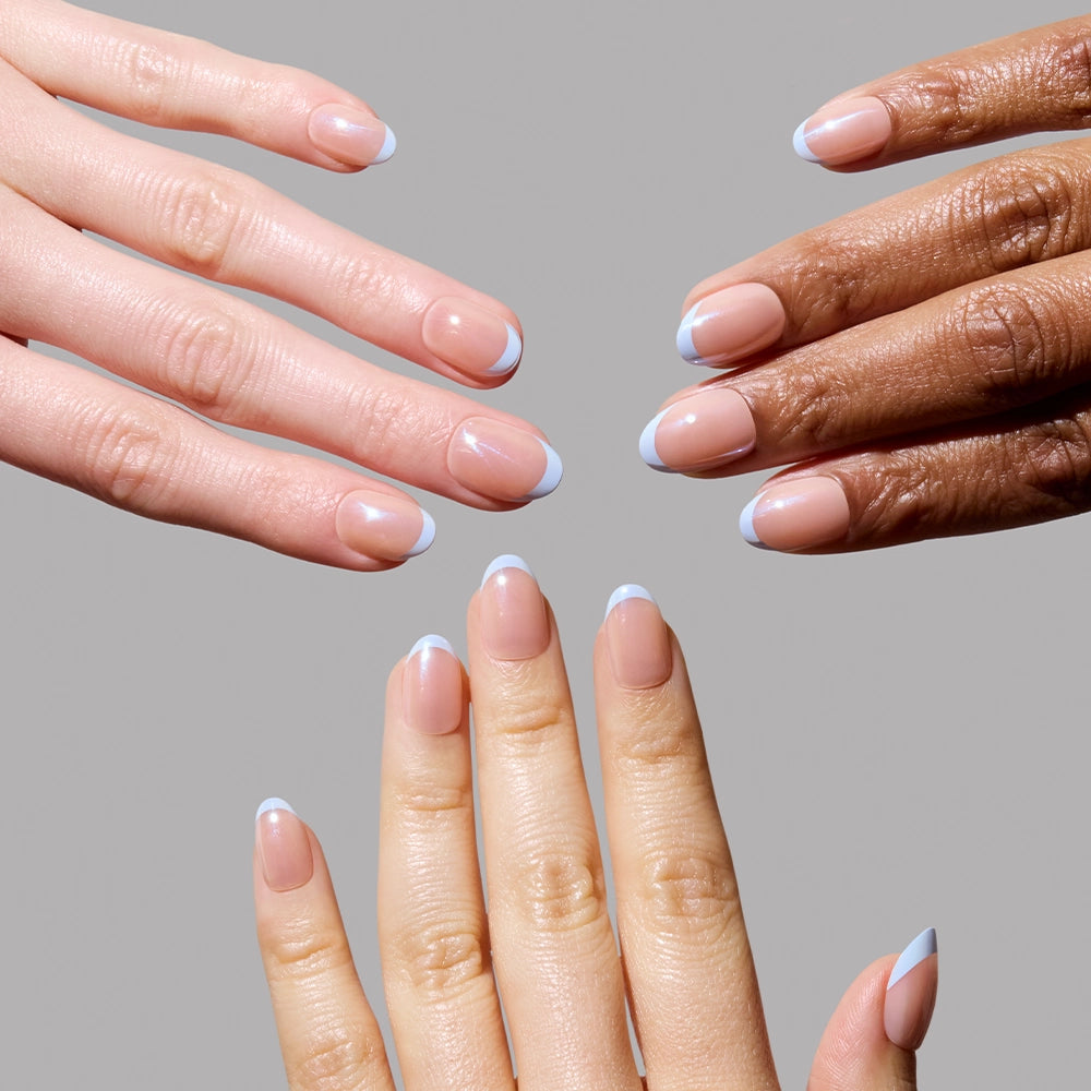 Three hands with different skin tones showcase glamnetics Into Blue salon-quality press-on nails, featuring a nude base and periwinkle micro French tips, against a plain gray background. - Product image