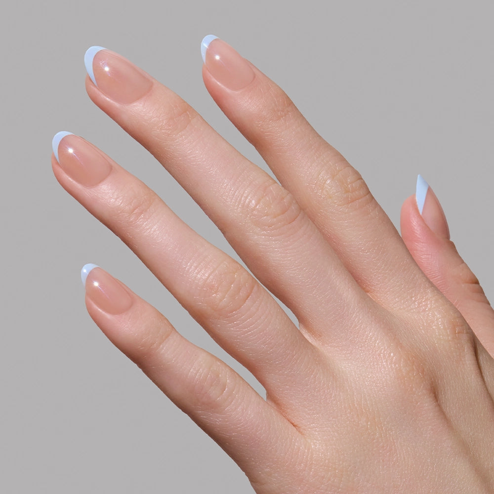 A hand with light skin and neatly manicured nails features glamnetics Into Blue salon-quality periwinkle micro French tips, shown against a plain gray background. - Product image