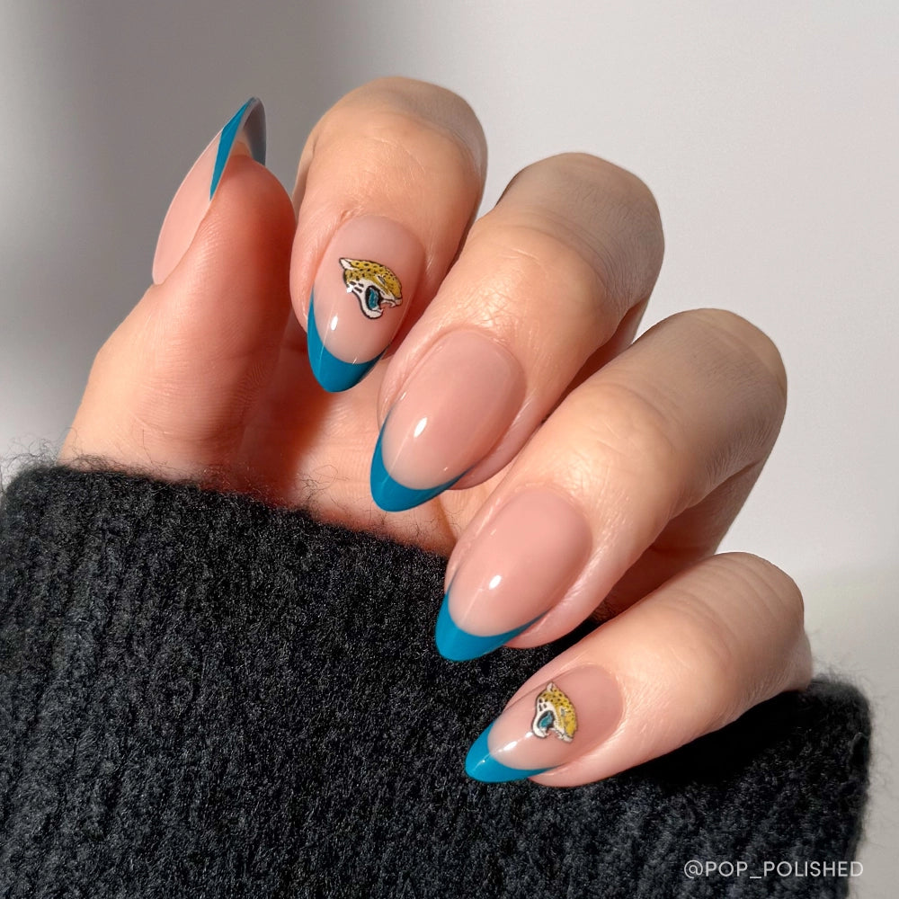A hand shows off the glamnetic Jacksonville Jaguars Press-On Nail Set with blue French tips and eye-shaped nail art accents, paired with a black sweater—an elegant update for almond mani lovers.
