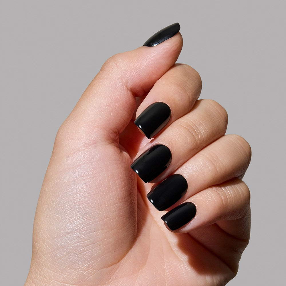 A hand with glossy squoval nails painted in glamnetics Jet Black is held against a plain light gray background. - Product image