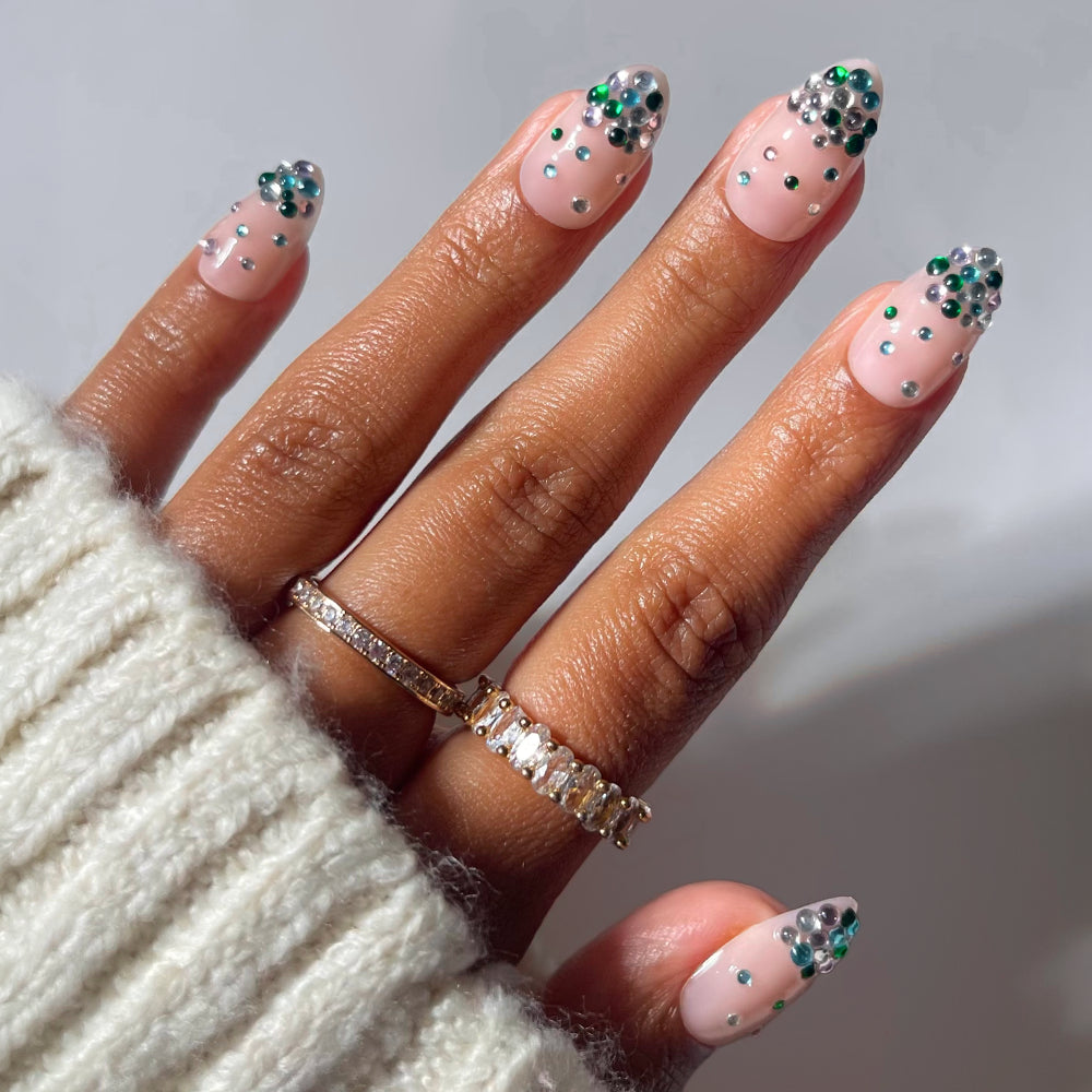 Glamnetic Jewel Thief press-on nails in a short, almond-shaped pale pink, accented with small green and clear crystals.