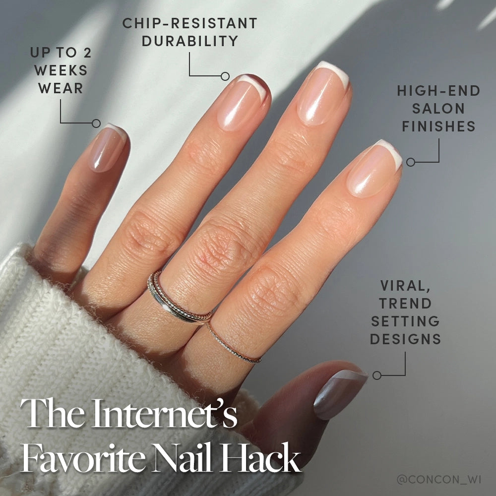 A hand with short squoval French tip nails from glamnetic’s La Perle set is shown in natural light with delicate rings. The text highlights up to two weeks’ chip-resistant wear and trendy designs. - Product image