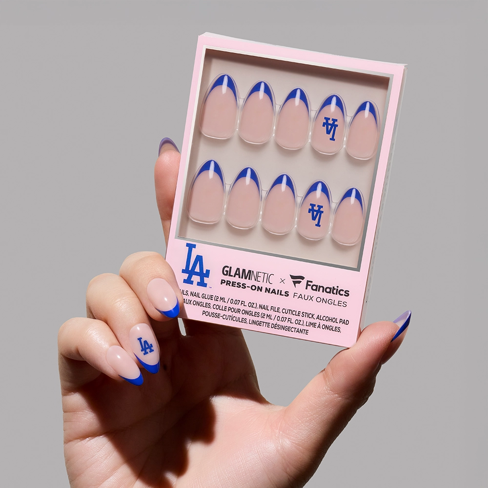 A hand with glamnetic Los Angeles Dodgers Press-On Nails featuring blue French tips and the LA Dodgers logo holds a GLAMNETIC x Fanatics box, displaying the Dodgers set with ten press-on nails and sporty packaging.
