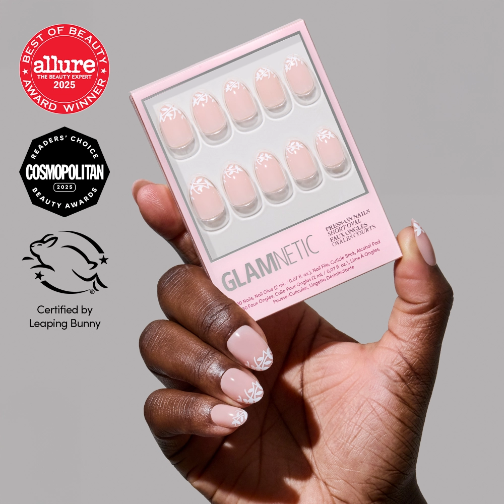 A hand with soft-romance, light pink Love Preserved nails by glamnetic, featuring a white leaf design, holds the matching press-on nail box. Award logos for Allure, Cosmopolitan, and Leaping Bunny appear on the left.