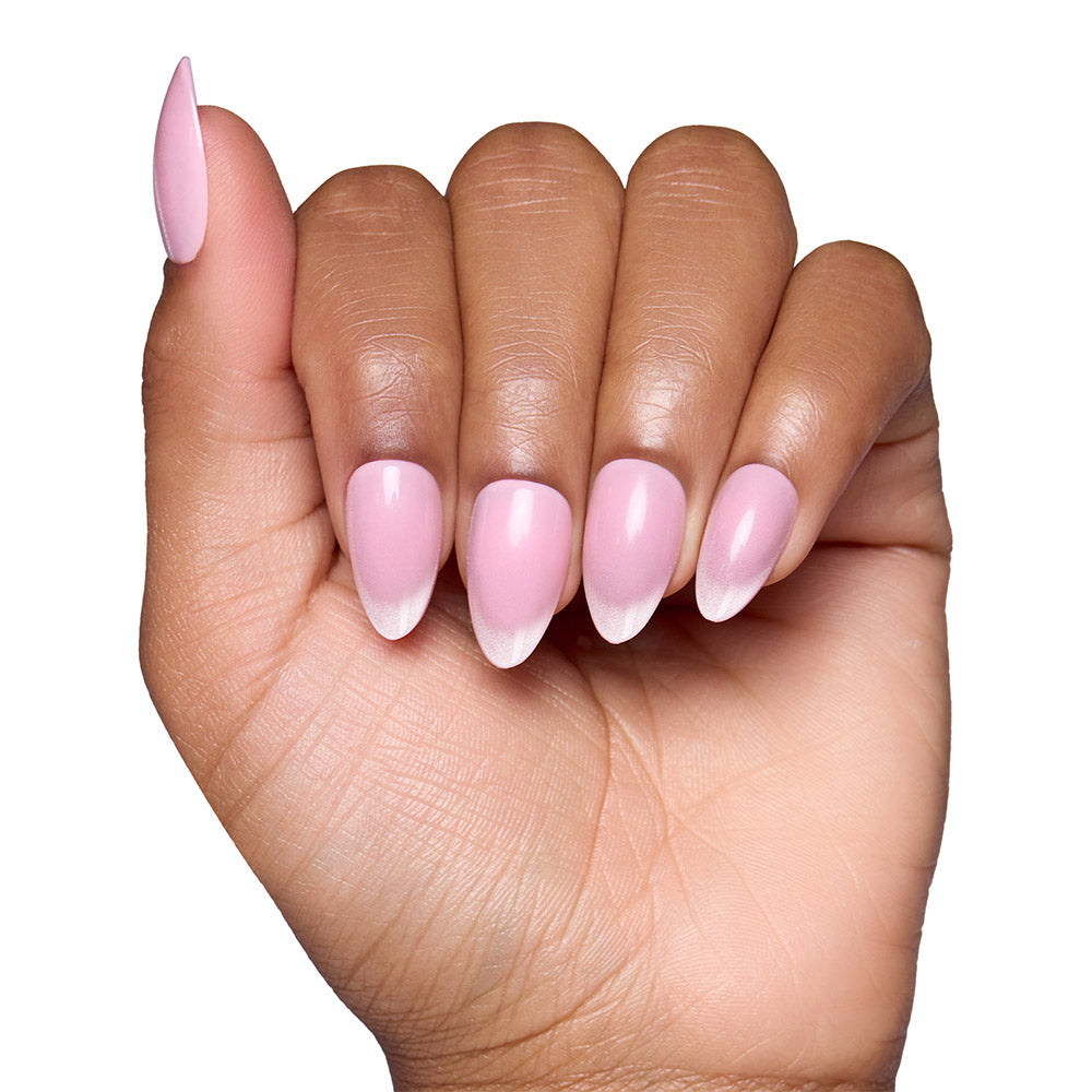 A hand with medium brown skin shows off long, almond nails painted in glamnetic’s Lovers Blush—a glossy, blush-pink shade—with a subtle white ombre at the tips, set against a white background. - Product image