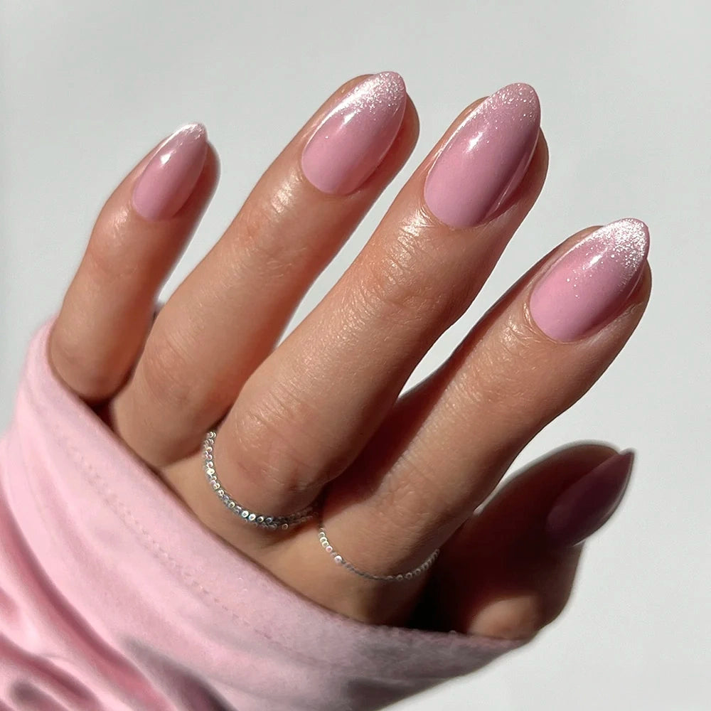 Hand with short almond nails wearing Lovers Blush, featuring a glossy, light pink polish with a subtle glitter gradient at the tips.