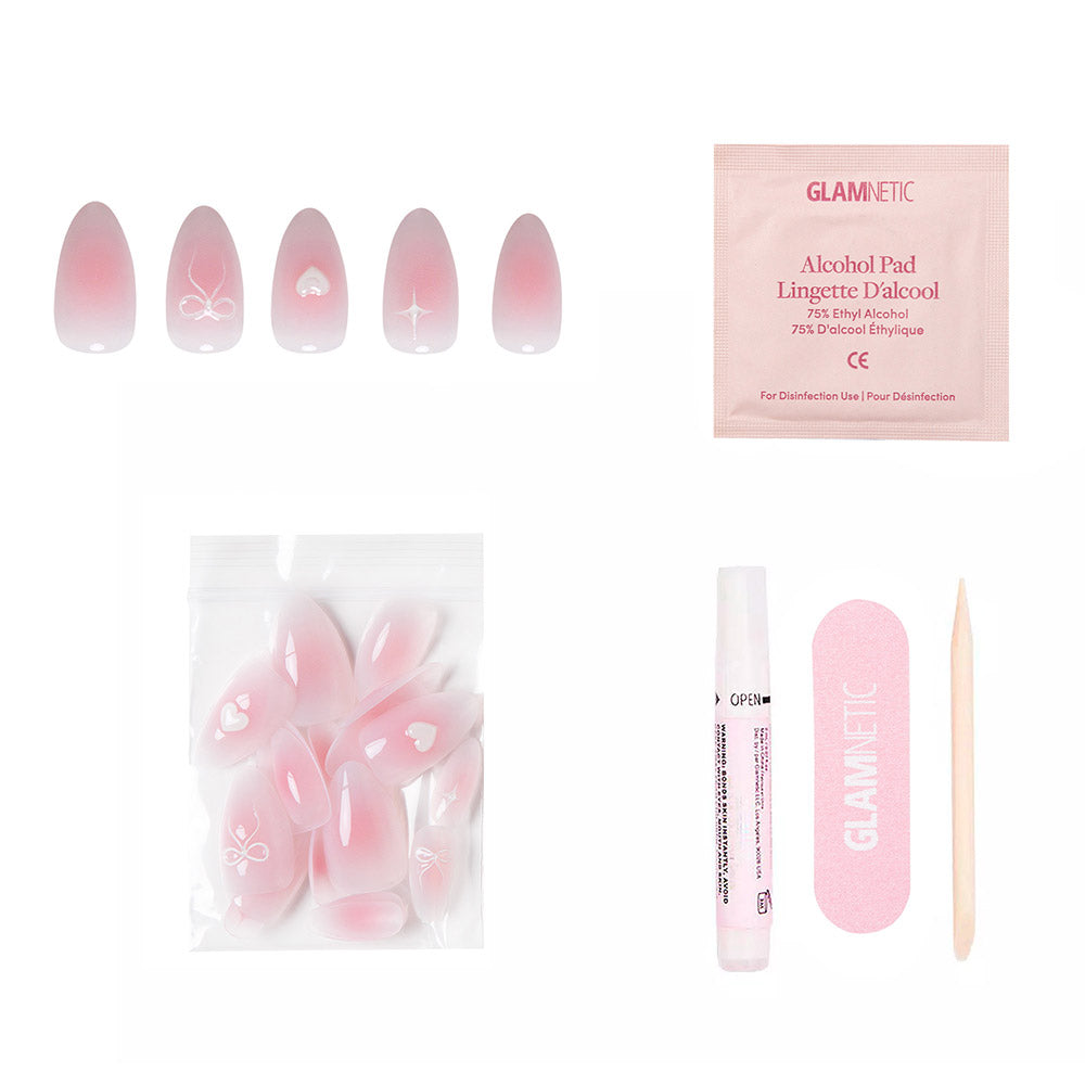 The glamnetic Lovers Knot press-on nail kit features short almond, semi-transparent pink nails with white floral designs and raised bows. Kit includes an alcohol pad, extra nails, glue pen, pink file, and wooden cuticle stick. - Product image