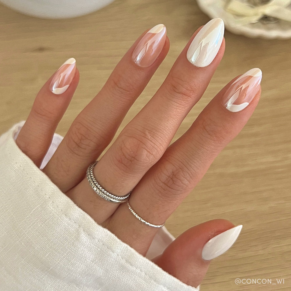 Lovey Dovey by glamnetic features almond nails with an elegant, minimalist white and beige design, combining abstract, geometric, and marble patterns. Two delicate silver rings accent the look.