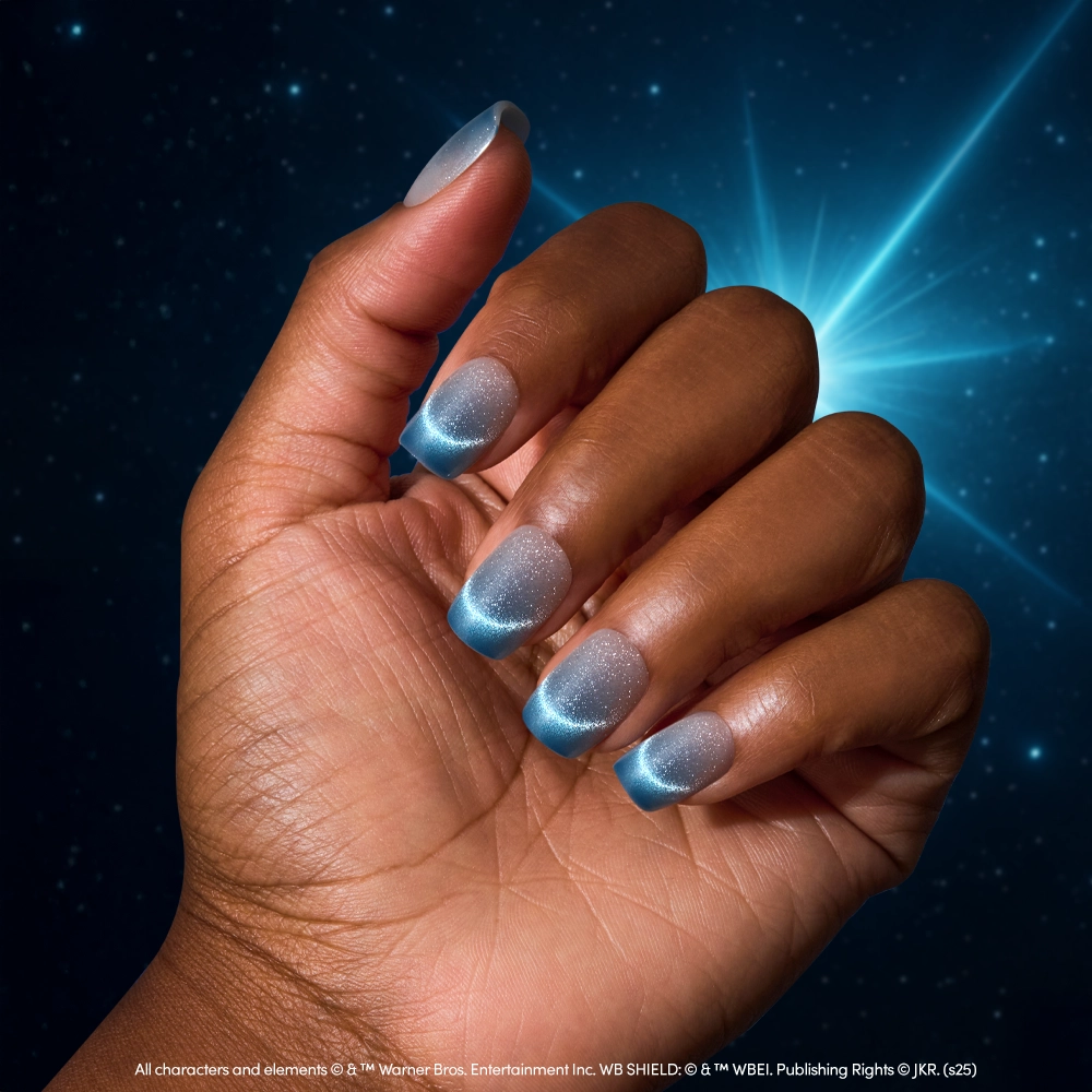 A hand with short, almond-shaped nails features a velvet blue gradient manicure with shimmery silver tones, set against a dark blue background and glowing light burst—perfect for the glamnetic Lumos Nail Set. - Product image