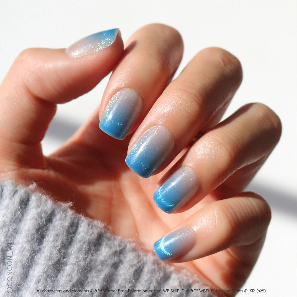 A hand with medium-length velvet blue gradient nails featuring a pale white-to-blue ombre, showcased by someone in a light gray sweater, highlights the Lumos set from glamnetic for an enchanting manicure. - Product image