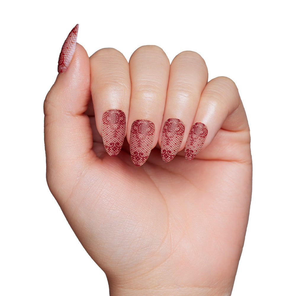 A hand with long, almond-shaped Lydia nails by glamnetic, featuring a 3D red lace design inspired by Beetlejuice’s Lydia Deetz, shown against a white background. - Product image