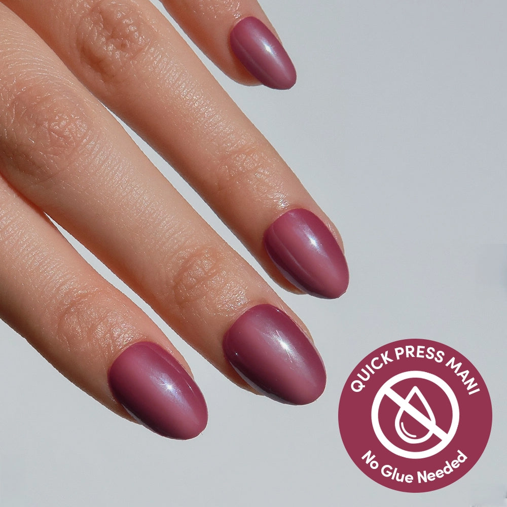 A hand with neatly manicured glamnetic Mauve Muse matte press-on nails. A circular icon in the corner reads “QUICK PRESS MANI - No Glue Needed.”.