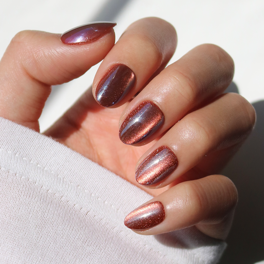 A hand with neatly manicured nails painted in glamnetic’s Magnetic Moscow—a shiny, metallic rose gold magnetic cat-eye polish—shown against a bright, neutral background; these dazzling nails capture the light beautifully and elevate any look.