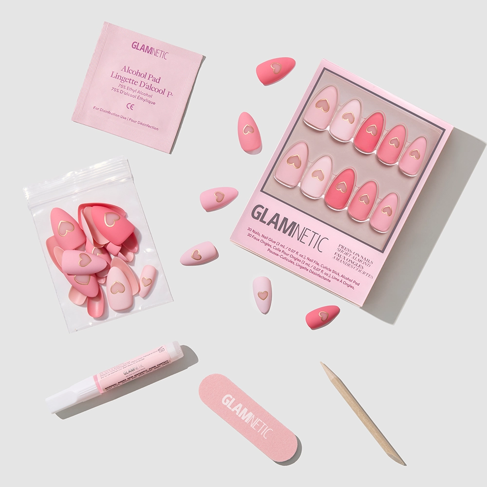 The glamnetic Matte in Love set features matte pink and red short almond press-on nails with gold heart cutouts, plus glue, a wooden cuticle stick, nail file, alcohol pad, and spare nails—all in signature glamnetic packaging. - Product image