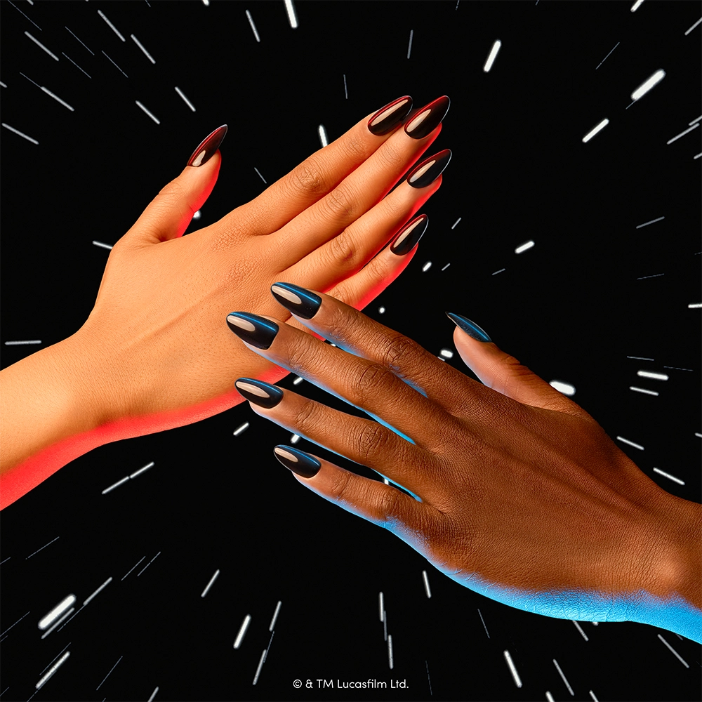 Two hands—one light-skinned and one dark-skinned—each adorned with glamnetic’s “May The Force Be With You” STAR WARS press-on nails, reach toward each other against a black background streaked with white lines like stars in motion. The sleek velvet top coat on every nail creates a striking contrast, evoking the dramatic sweep of lightsabers through space. - Product image