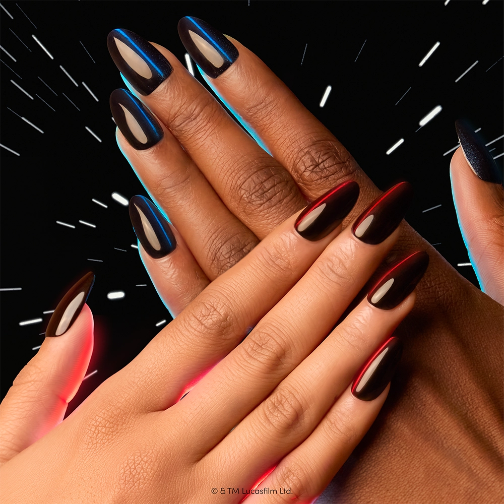 Two hands with long, shiny, red and blue ombre nails overlap against a dark background streaked with white light, capturing the cosmic vibe of glamnetic’s May The Force Be With You STAR WARS press-on nails set. - Product image