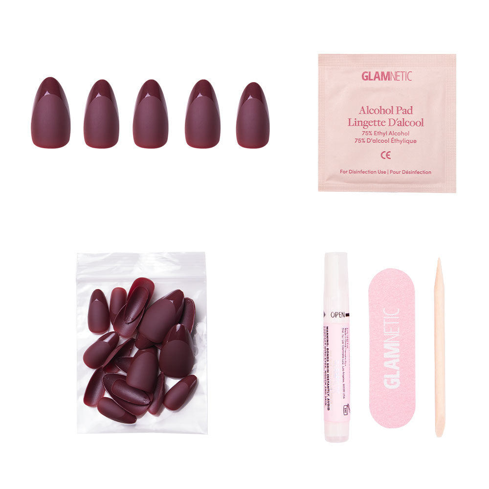 The Merlot nail set by glamnetic includes short almond-shaped burgundy matte press-on nails, extra nails, nail glue, an alcohol pad, a pink nail file, and a wooden cuticle stick—all arranged on a white background. - Product image