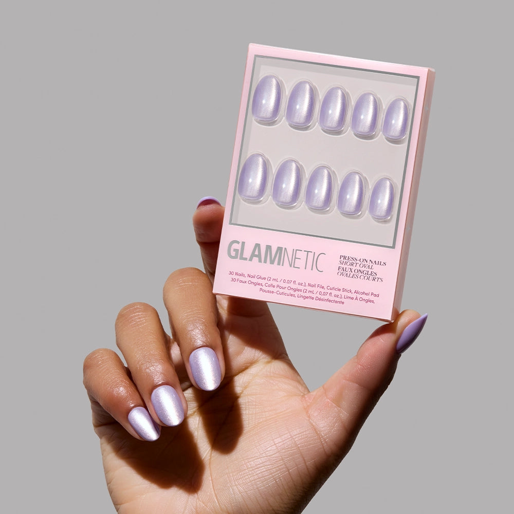 A hand with shimmery, iridescent purple Mermaids Tail press-on nails holds a glamnetic box featuring the matching set of nails against a plain grey background. - Product image