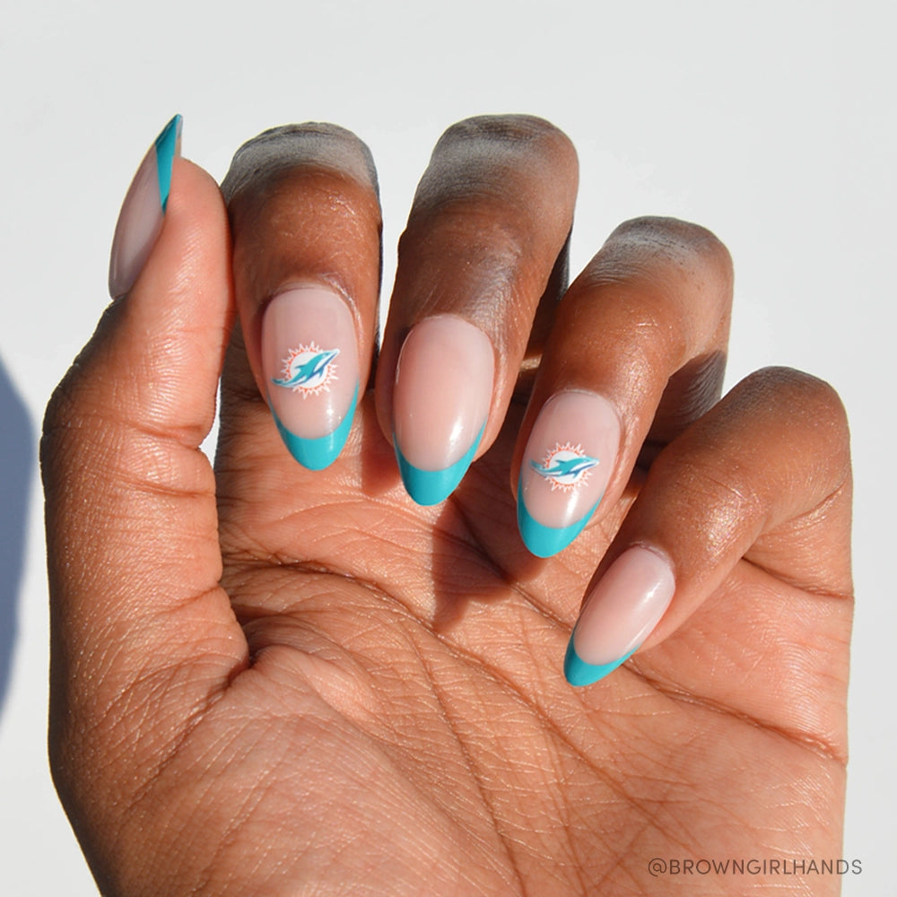 The Miami Dolphins Press-On Nail Set by glamnetic features almond-shaped nails with turquoise French tips and two nude nails decorated with the Dolphins logo, all shown against a white background. - Product image