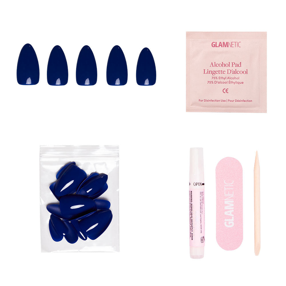 The glamnetic Midnight Blue set includes vegan, cruelty-free navy press-on nails, an alcohol pad, extra nails, nail glue, a pink nail file, and a wooden cuticle stick—all beautifully arranged on a white background. - Product image